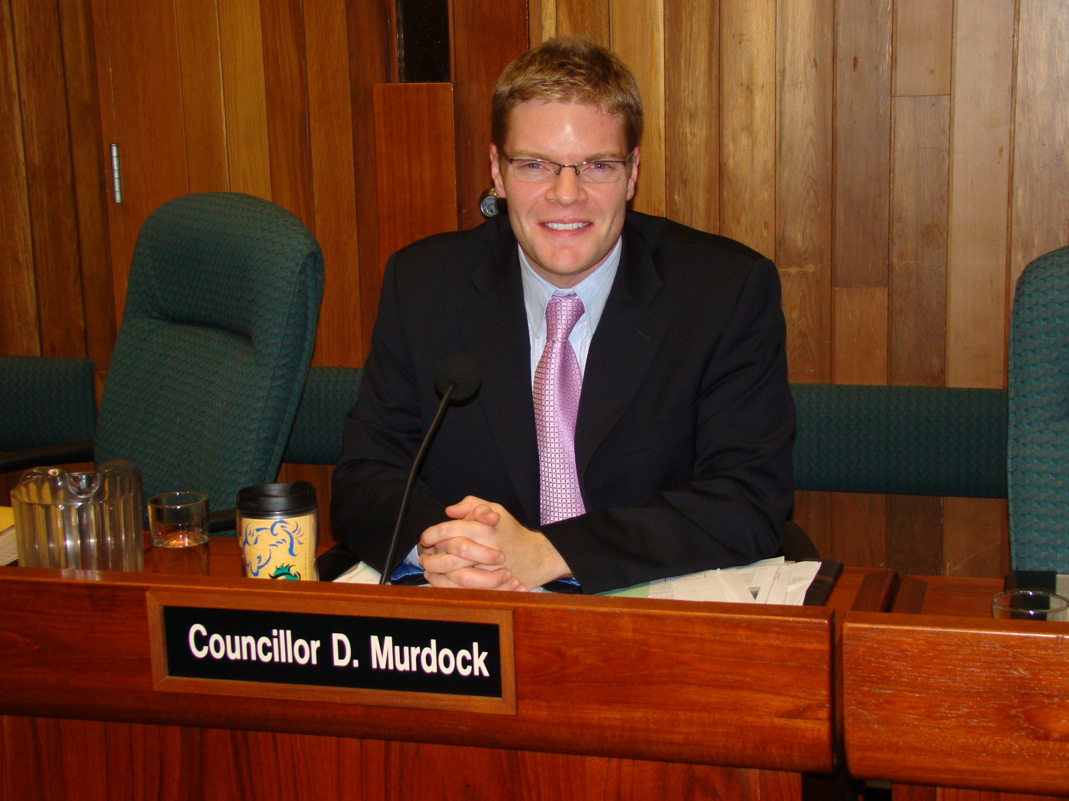 Dean sits at a desk behind a plaque that reads "Councillor D. Murdock"