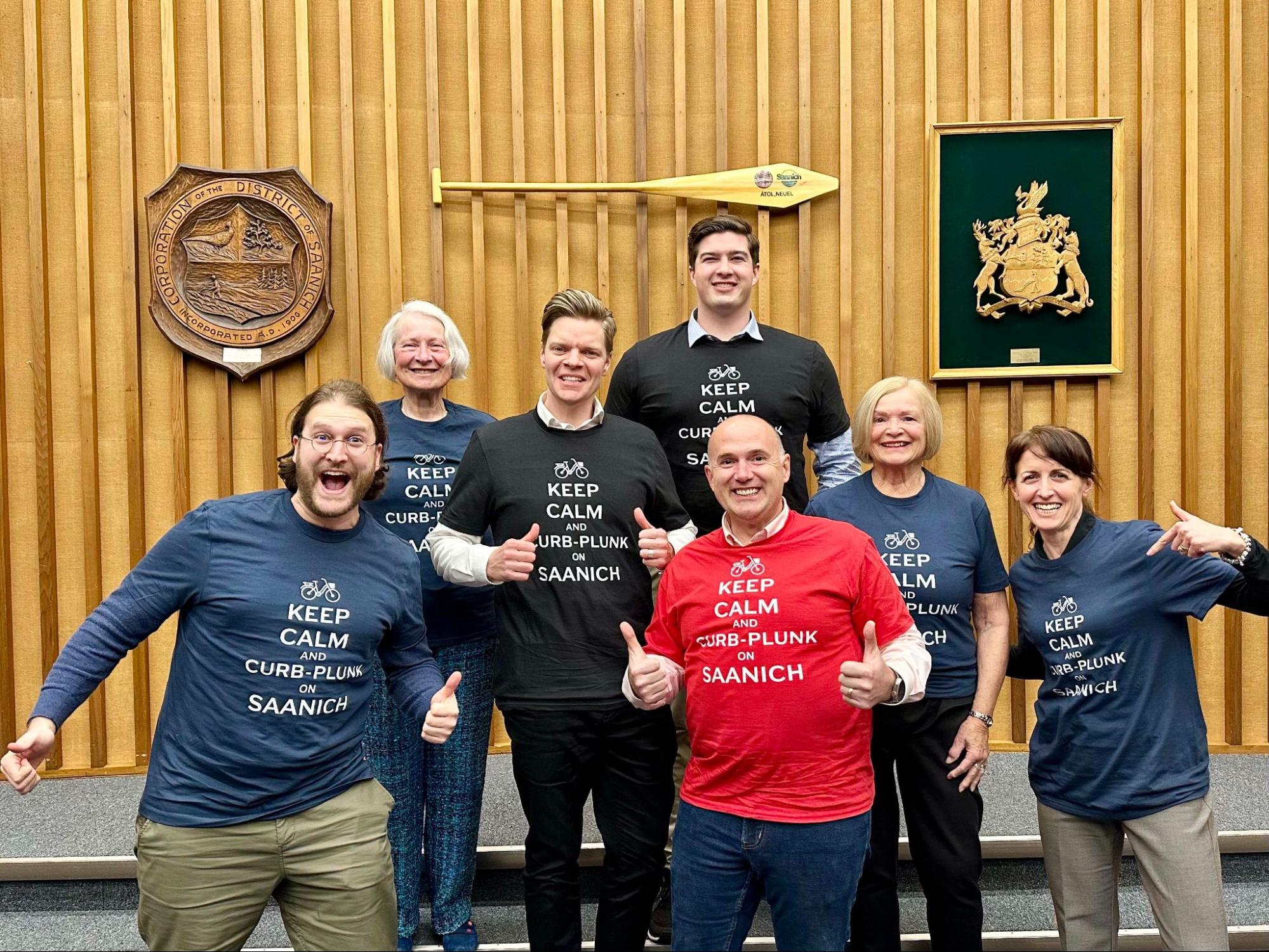 Dean stands in the middle of six other Council members (Teale, Karen, Zac, Colin, Susan, and Mena) smiling with shirts that read "Keep Calm and Curb-Plunk On Saanich"