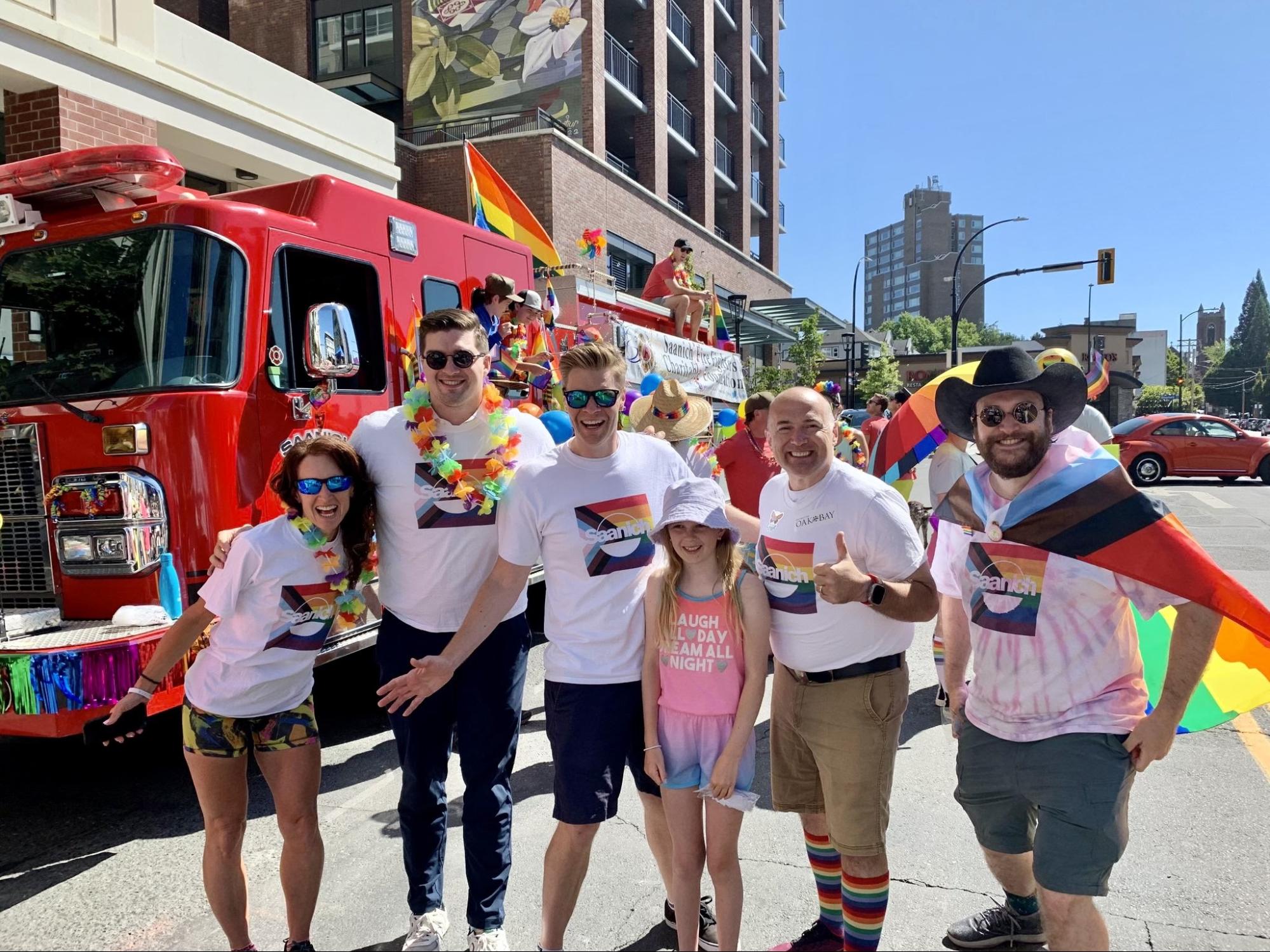 Dean stands with Mena, Zac, Colin and Teale (four other council members) and his daughter wearing Saanich pride shirts as they prepare to march in a pride parade.