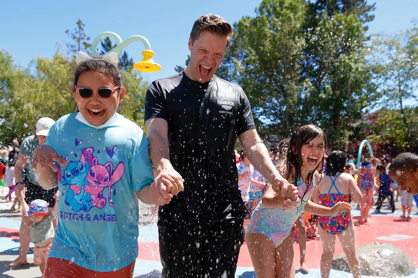 Dean holds hands with two young people as they run through a splash park.